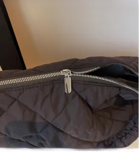 Detailed close-up of smooth silver zipper and black quilted diamond pattern on tote bag