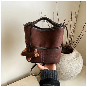 Detail of dark brown suede bucket bag with contrast stitching and plush dog charm