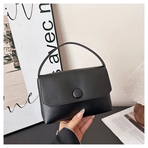 Detail of a minimalist black leather handbag with a round buckle and thin top handle