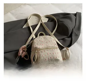 Close-up of stylish tweed mini backpack with pink charm and gold zipper detail