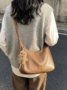 Retro brown half-moon hobo bag with teddy charm shown on shoulder in street style