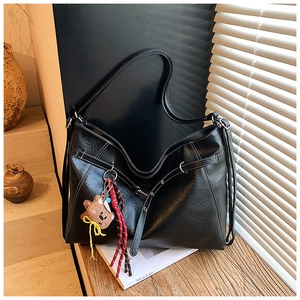 Detail of black faux leather tote bag featuring contrast white stitching and bear charm