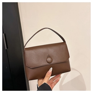 Detailed close-up of dark brown leather handbag with a circular buckle and top handle
