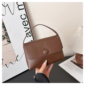 Detail of a brown leather square handbag with pebble texture and leather button closure