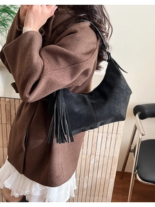 Detail of black hobo bag with long fringe tassels shown from a side view on shoulder