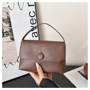 Detail of the litchi texture brown leather handbag with a top handle and flap closure