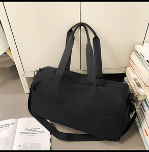 Close-up of black travel bag with dual handles and adjustable shoulder strap in home setting