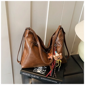 Detail of dark brown leather tote bag with white stitching and plush bear charm
