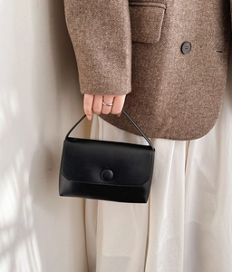 Detail of elegant black faux leather handbag with circular clasp and slim handle