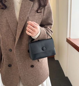 Detailed macro view of a black matte leather handbag featuring a round clasp and flip cover