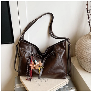 Detail of dark brown faux leather shoulder bag with vintage texture and plush bear charm