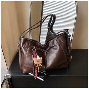 Detail of dark brown leather tote bag with contrast stitching and teddy bear charm