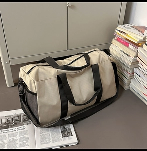 Macro shot of beige travel duffel bag with black handles and side mesh pocket detail
