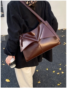 Dettaglio della borsa in pelle marrone con patta origami su modella in stile autunnale