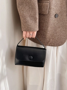 Minimalist black leather handbag with a large button closure held by a model in a blazer
