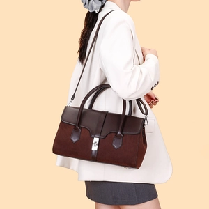 Detail of dark brown leather handbag with silver lock worn by model in white suit