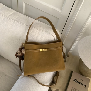 Détail du sac en daim avec fermoir doré et charm ours en tricot sur un canapé beige