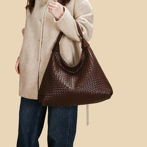 Borsa hobo in pelle intrecciata marrone indossata da modella con cappotto beige e jeans