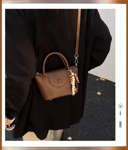 Brown vintage leather bucket bag featuring wooden bead decor and a long shoulder strap