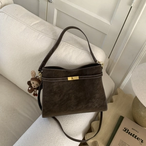 Détail du sac mat marron foncé avec fermoir doré, surpiqûres blanches et charme singe