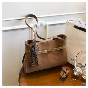 Detail of vintage brown tote bag featuring metal buckle strap and woven tassel pendant