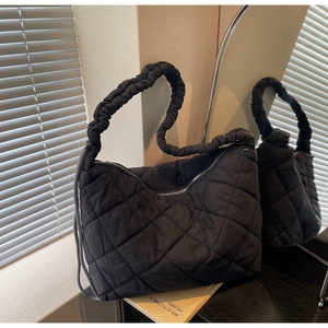 Detail of black quilted puffer tote bag featuring textured rhombic pattern and braided strap
