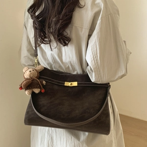 Détail du sac à bandoulière en daim marron foncé avec fermoir doré et charme d'ours