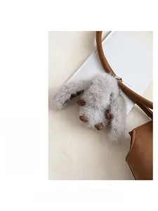 Détail d'un charmant lapin en peluche grise sur la poignée d'un sac en cuir marron
