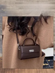 Gros plan détaillé du sac carré marron foncé avec fermoir argenté sur un manteau