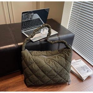 Detail of olive green quilted tote bag featuring a ruffled shoulder strap and zip closure