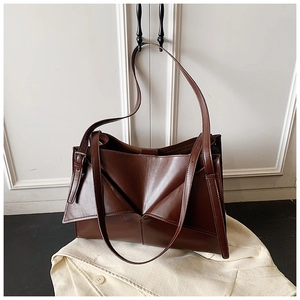 Dettaglio borsa tote in pelle marrone scuro con design geometrico appesa a porta bianca