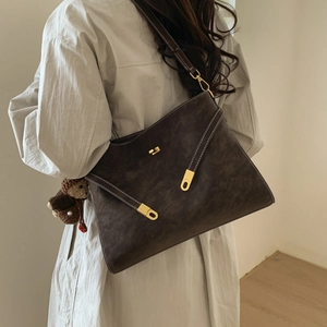 Détail du sac cabas en cuir marron foncé avec surpiqûres blanches et charme d'ours mignon