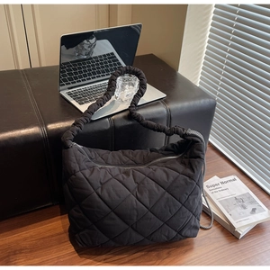 Detailed close-up of a black quilted tote bag with silver zipper and ruffled strap