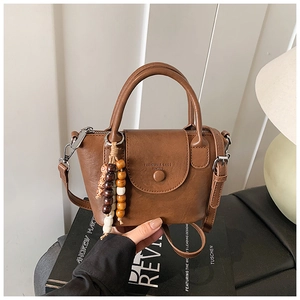 Detail view of a vintage brown leather handbag featuring unique wooden bead charms and handles