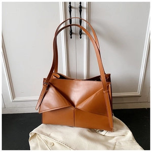 Dettaglio della borsa a spalla color caramello con design a pieghe geometriche su un blazer