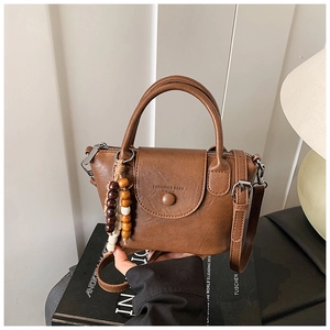 Detail of a brown leather shoulder bag with beaded fringe tassel and stamped logo text