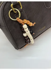 Close-up of brown pebbled leather handbag with colorful wooden bead tassel and gold hardware
