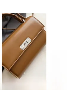 Detail of caramel brown leather handbag featuring a polished silver twist lock closure