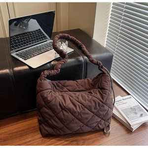 Detail of quilted dark brown tote bag with ruffled strap on office desk setting