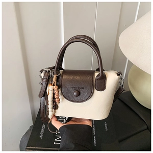 Detail of two-tone faux leather crossbody bag with wooden bead charm and top handle