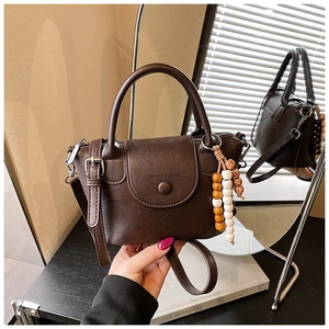 Close-up of dark brown soft leather handbag featuring wooden bead charm and flap closure