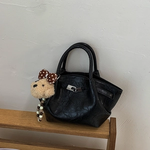 Detail view of glossy black pleated bucket bag with silver metal lock and puppy charm