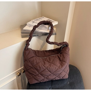 Detail of dark brown quilted tote bag with a ruffled strap on a cozy grey seat