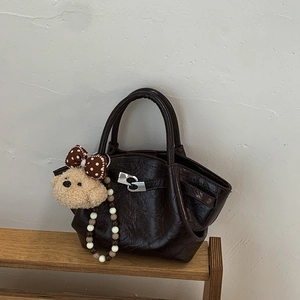Detail of a shiny dark brown bucket bag with double handles and a cute bear charm on a wood shelf