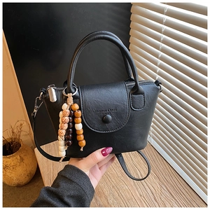 Close-up of black matte leather handbag featuring wooden bead charm and crossbody strap