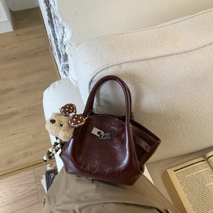 Detail of burgundy bucket bag with glossy texture and cute plush bear charm accessory