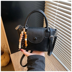 Detail of minimalist black PU leather handbag with beaded charm in cozy indoor setting