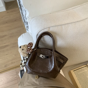 Detail of dark brown bucket bag with plush bear charm and beaded chain on a sofa