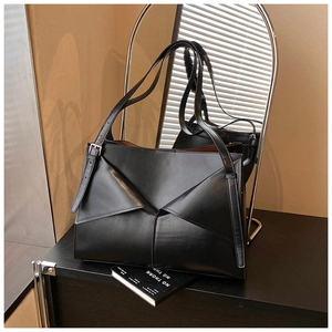 Dettaglio della borsa in pelle nera con pieghe geometriche su supporto minimalista