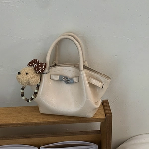 Close-up of cream leather bucket bag with silver twist lock and bear charm